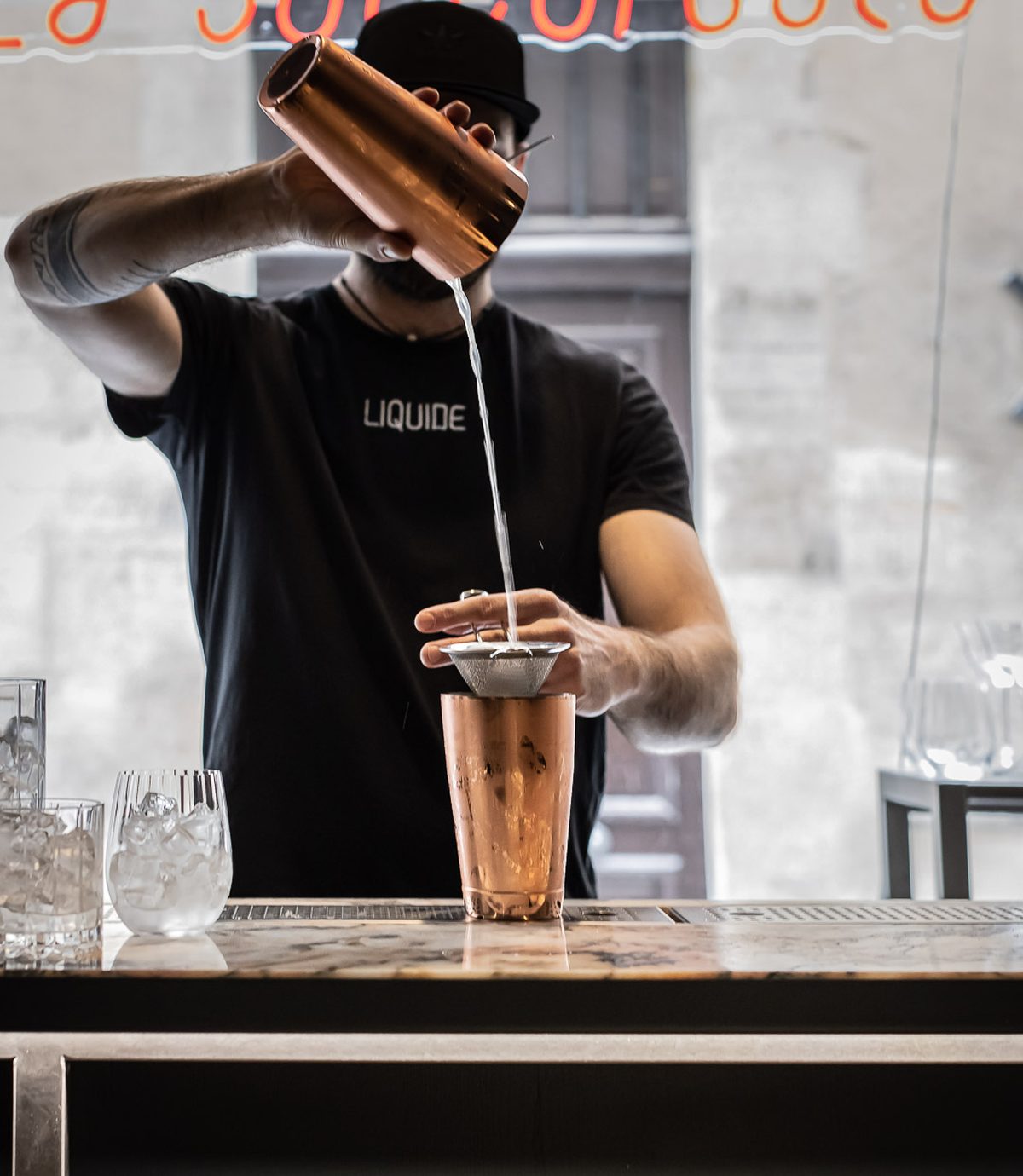 Le bar de La Succursale, la salle privatisable de Liquide : un cocktail préparé au comptoir de marbre sous l’enseigne au néon, Paris 1er
